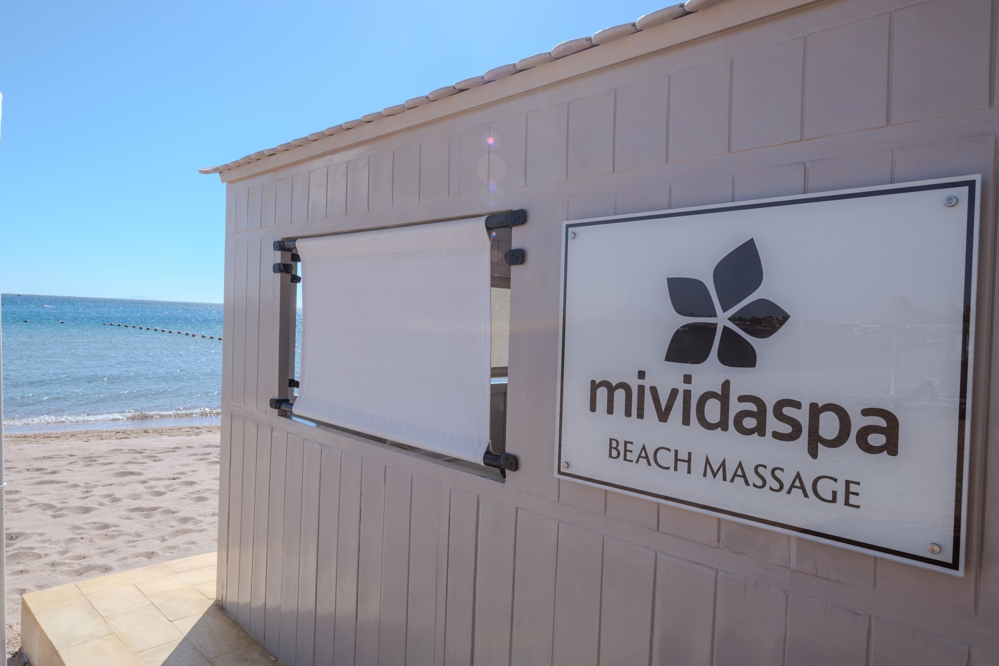 Letrero de un servicio de masajes en la playa en un edificio con vista al océano.