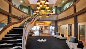 A spacious lobby with a central staircase, a chandelier, and seating areas.