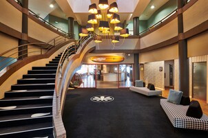 A spacious lobby with a central staircase, a chandelier, and seating areas.