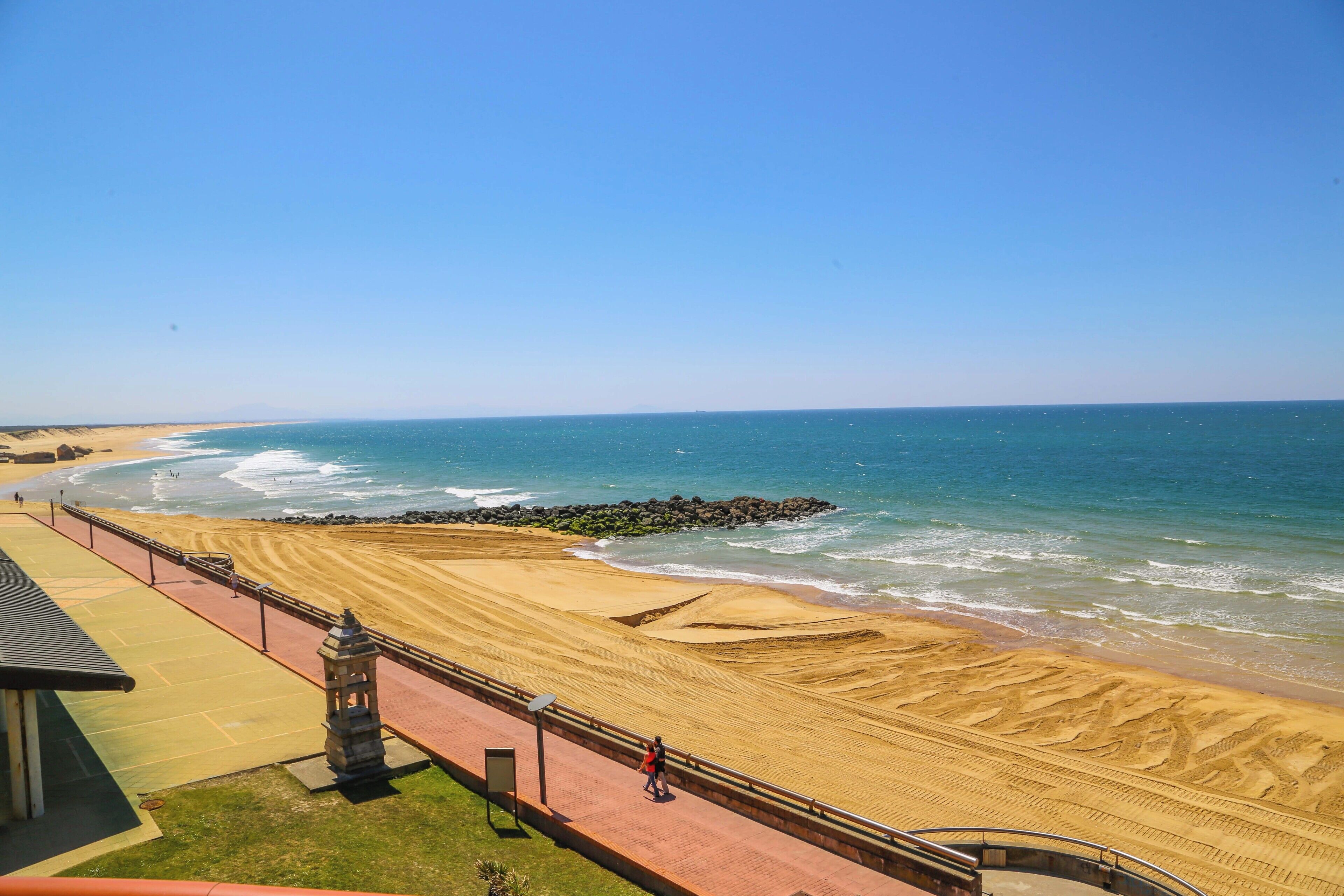 A beach with a paved walkway, a stone structure, and a view of the ocean.