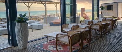 Un salon de plage doté de meubles en osier, d’un tapis à motifs et offrant une vue sur l’océan.