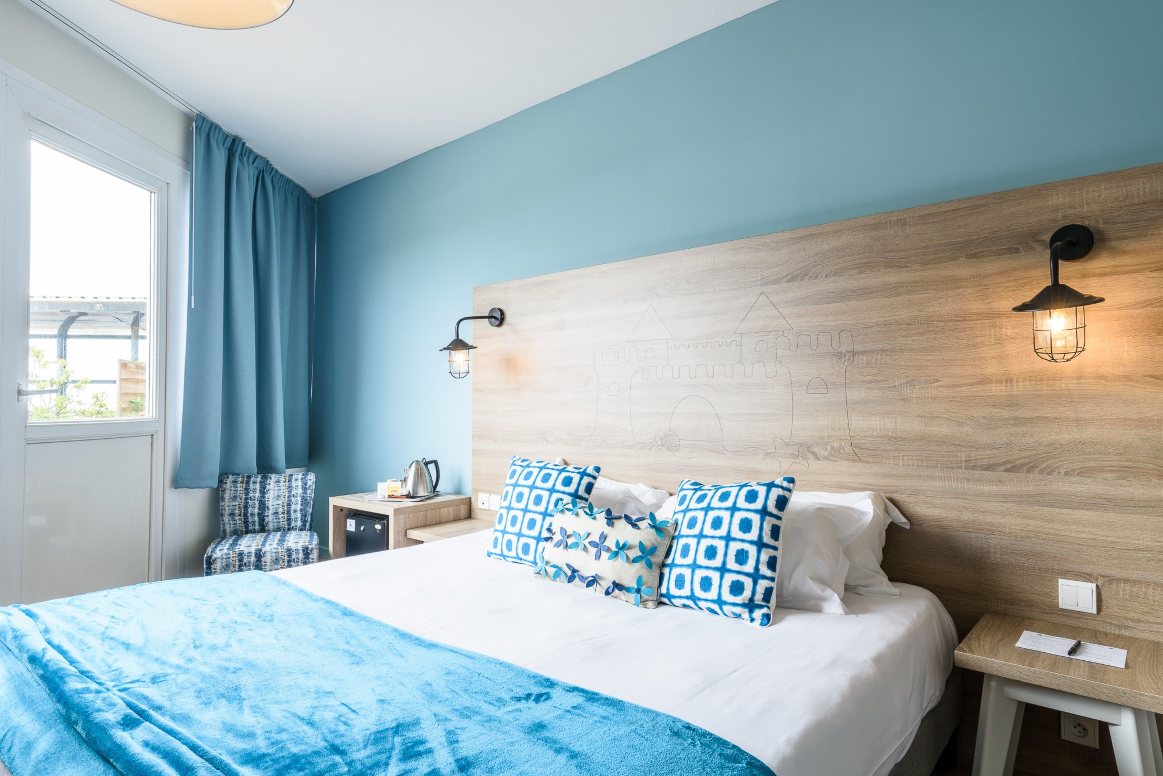 A bedroom with a large bed, a wooden headboard, two bedside tables, a nightstand, a window with curtains, and a wall-mounted light fixture.
