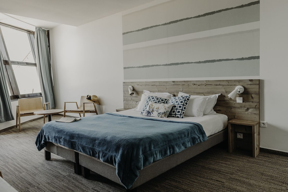A modern bedroom with a large bed, a wooden headboard, and a view of the outdoors through a window.