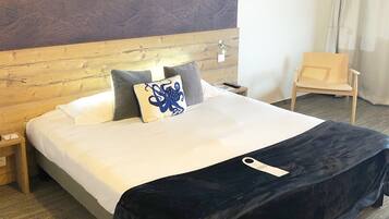 A hotel room with a wooden headboard, a bed with white linens, a dark blue throw blanket, and a single pillow with a blue design.