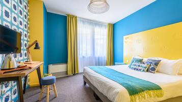 Ein Hotelzimmer mit Bett, Schreibtisch mit Lampe, Fernseher und einem Fenster mit Vorhängen.