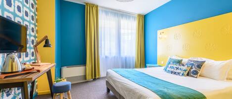 Una habitación de hotel con cama, escritorio con lámpara, televisión y ventana con cortinas.