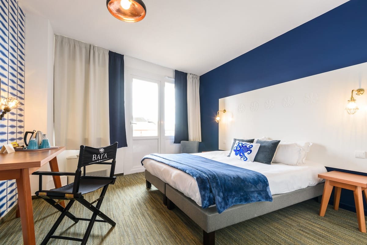 A hotel room with a bed, a desk, a chair, and a window with curtains.