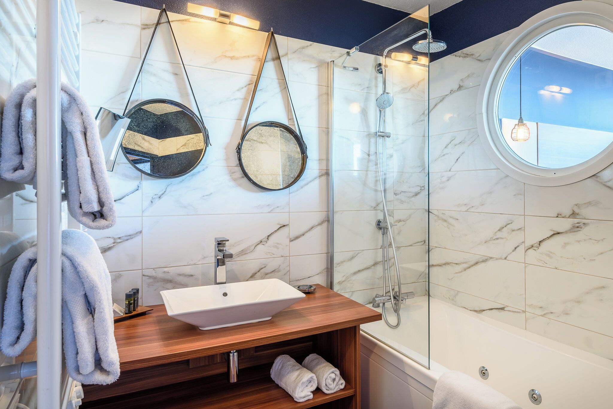 Ein Badezimmer mit Marmorwand, einem Holzboden, einem Waschbecken, einer Dusche und zwei Spiegeln.