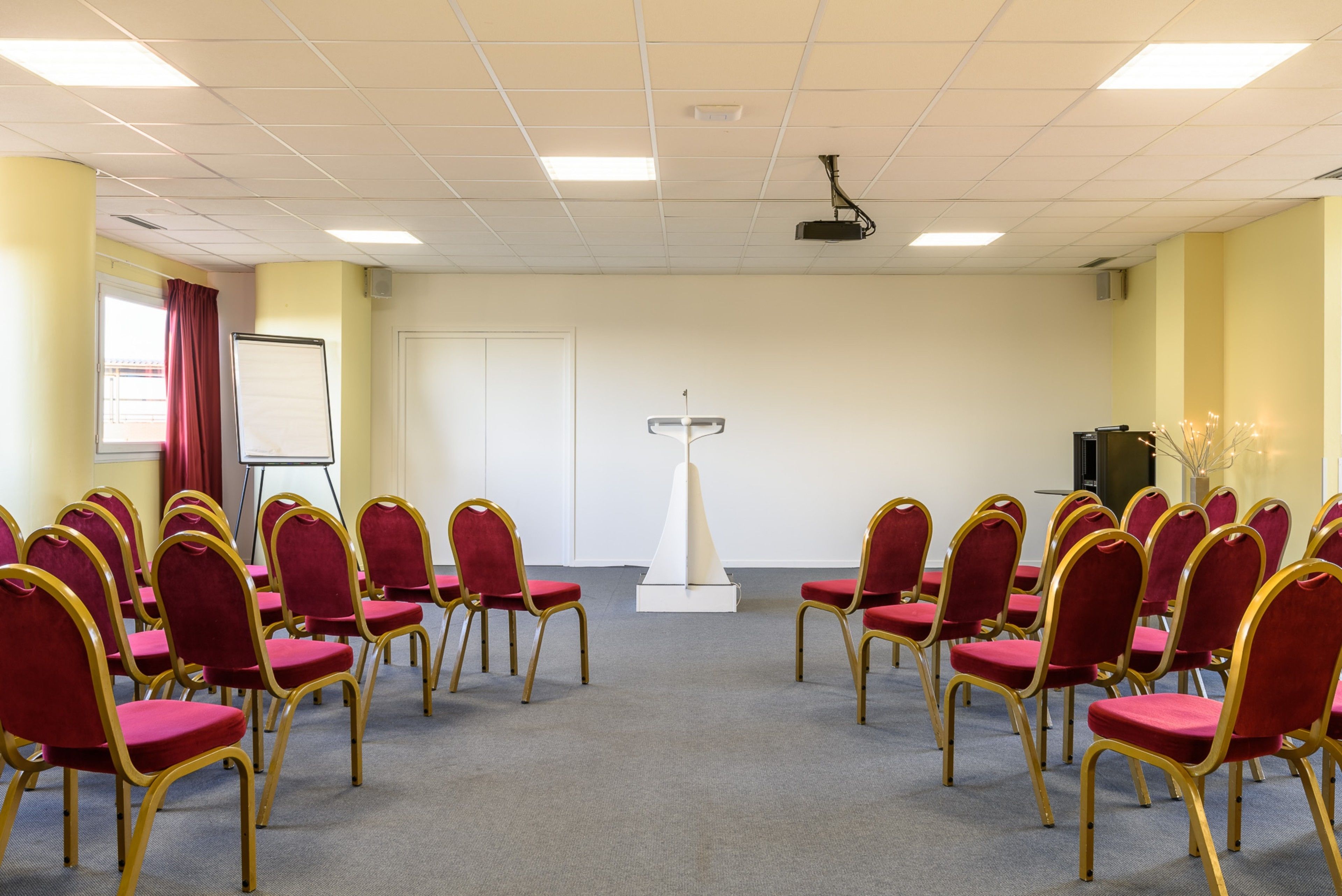 Une salle de conférence avec des rangées de chaises rouges et un pupitre au centre.