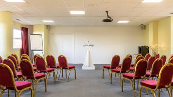 Une salle de conférence avec des rangées de chaises rouges et un pupitre au centre.
