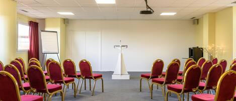 A conference room with rows of red chairs and a podium in the center.