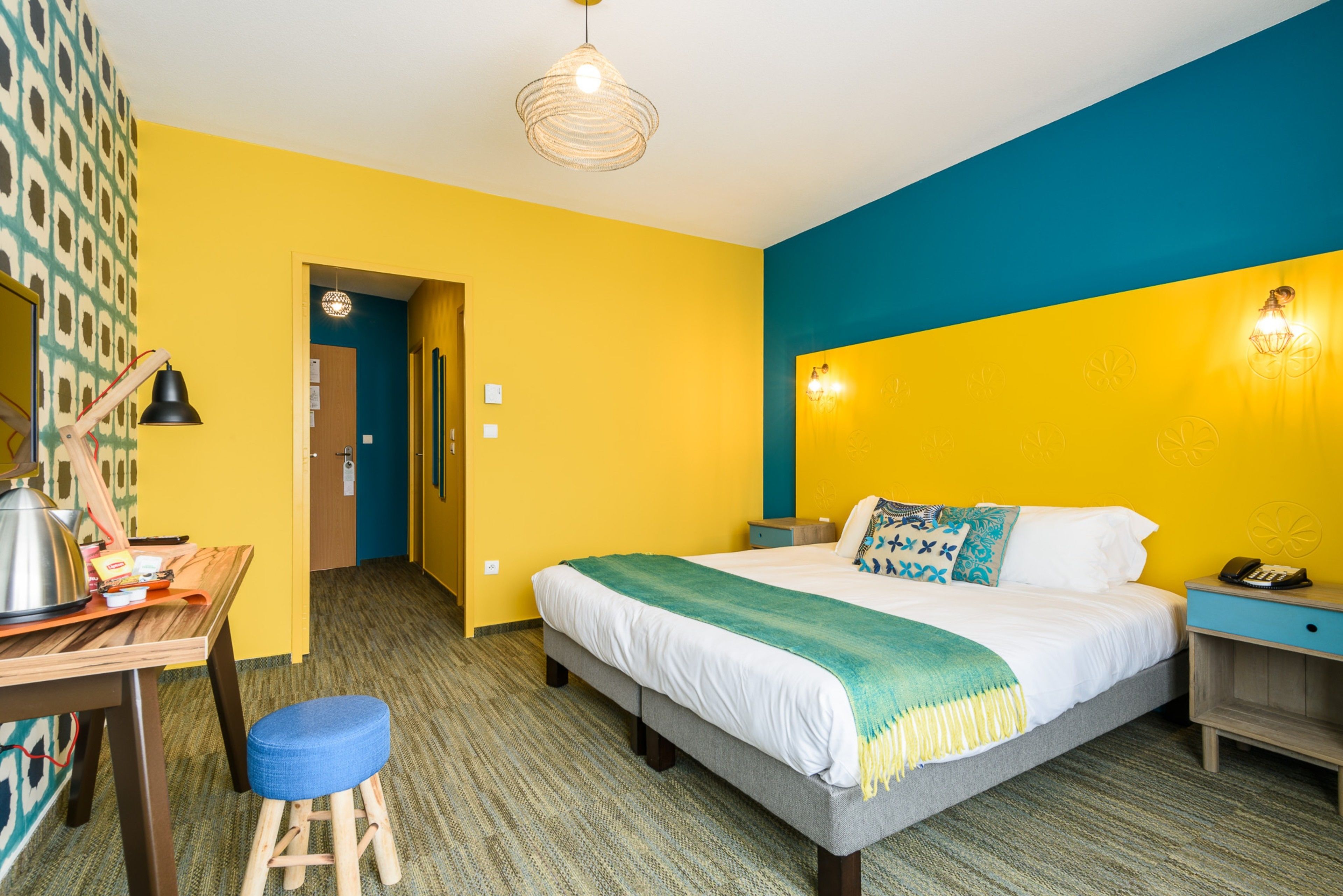 Quarto de hotel com cama, escrivaninha, cadeira e abajur.