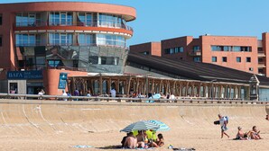 A beachfront hotel with a curved building, a pool area, and a beach in the foreground.