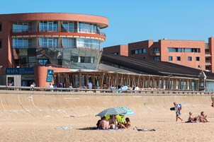 A beachfront hotel with a curved building, a pool area, and a beach in the foreground.