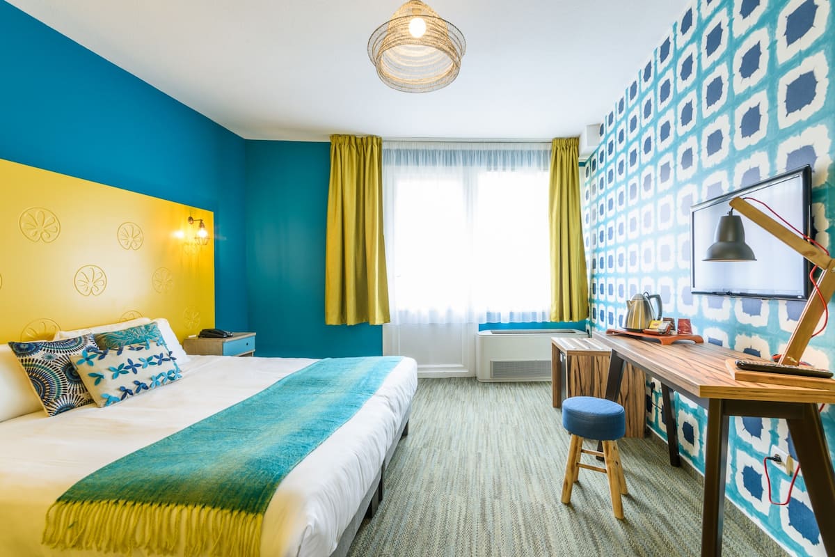 A hotel room with a bed, desk, and a patterned wall.