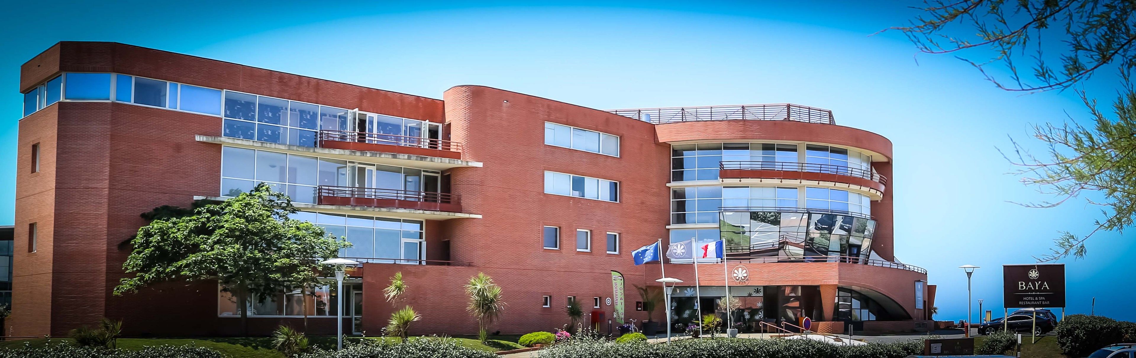A modern hotel with a curved facade, multiple balconies, and a rooftop terrace.