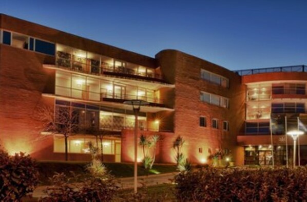 A multi-story hotel with a curved facade, balconies, and a well-lit entrance.