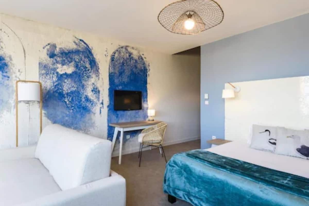 A hotel room with a bed, a desk, a chair, a television, and a lamp.
