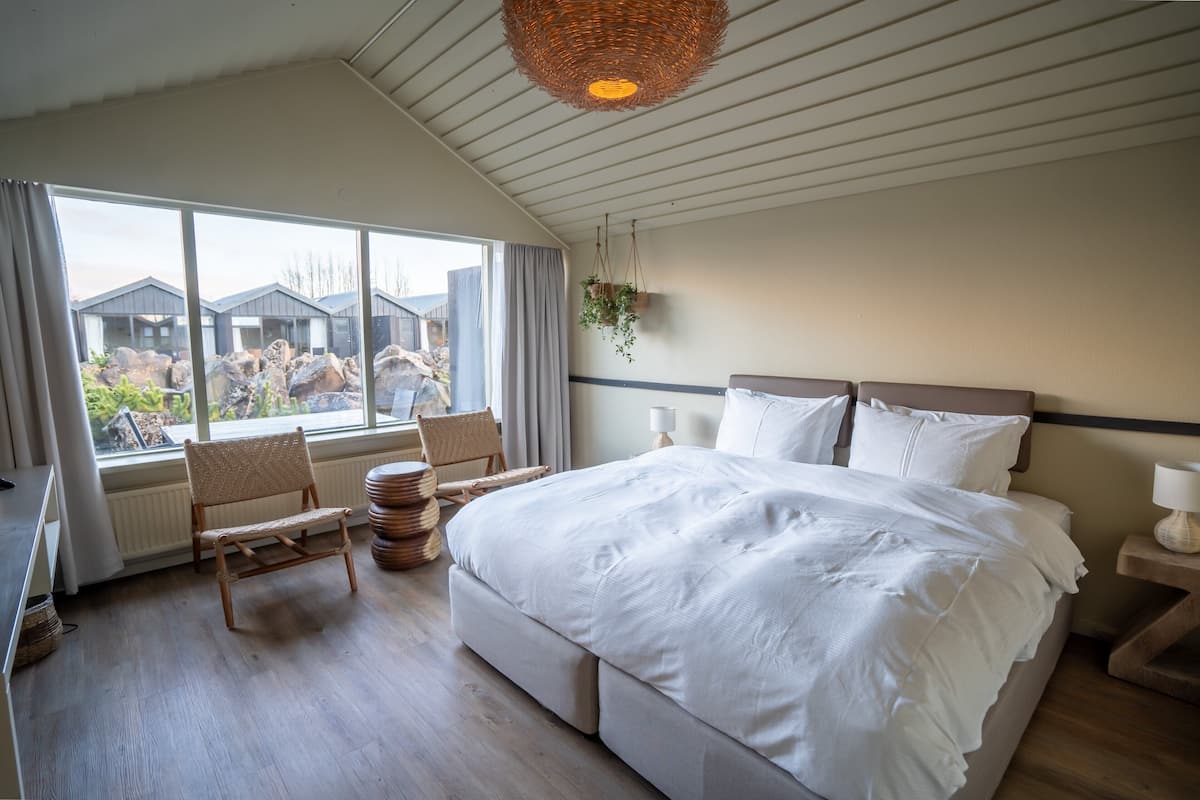Een slaapkamer met een groot bed, een raam met uitzicht op gebouwen, een hanglamp van riet en een stoel bij het raam.