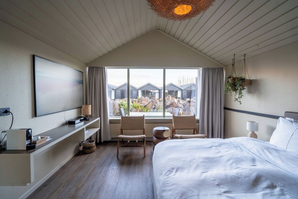 Une chambre d’hôtel avec un grand lit, un bureau avec un ordinateur, une télévision et une fenêtre donnant sur d’autres immeubles d’hôtels.