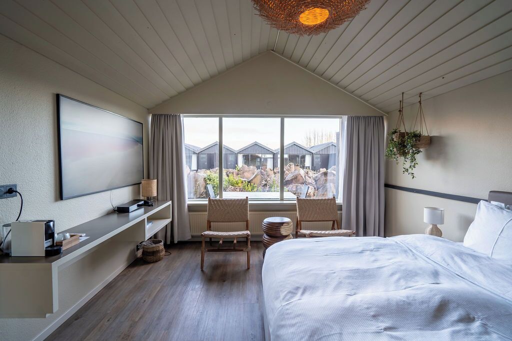 Una habitación de hotel con una cama grande, un escritorio con computadora, un televisor y una ventana con vistas a otros edificios de hotel.
