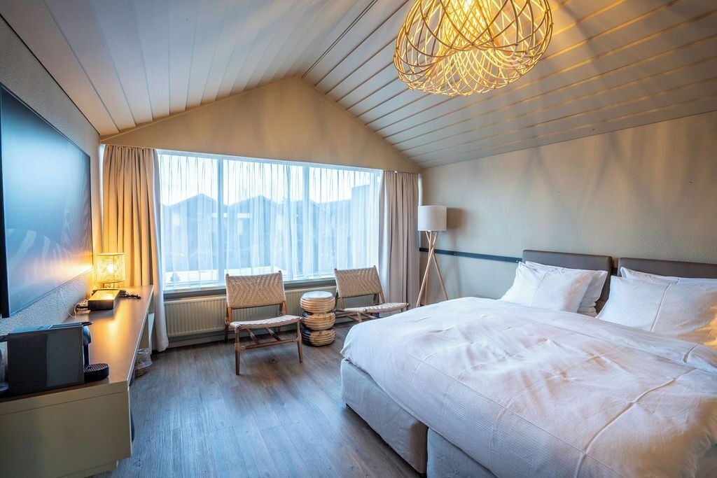 Habitación de hotel con una cama grande, un escritorio con lámpara, una silla y vistas al exterior a través de la ventana.