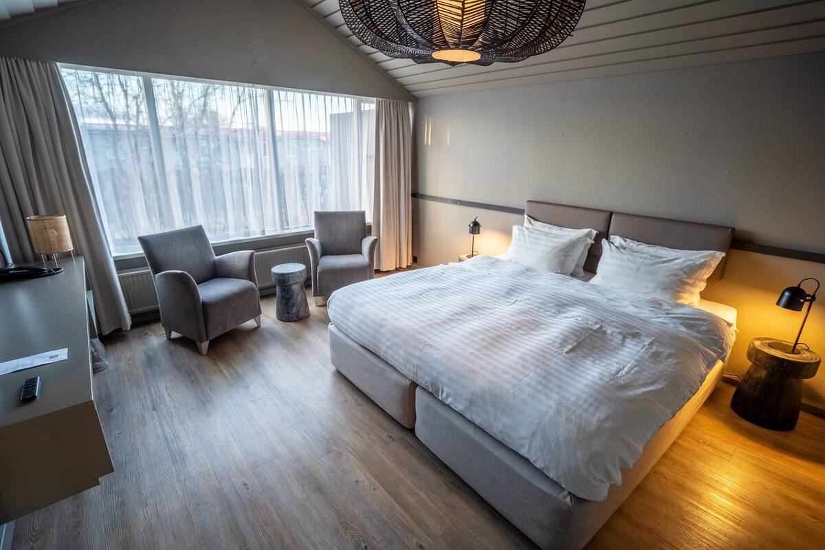 Een moderne hotelkamer met een groot bed, een stoel, een tafeltje en een lamp.