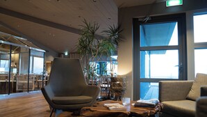 Een modern interieur met een houten vloer, twee grijze fauteuils, een houten bijzettafeltje en een groot raam.