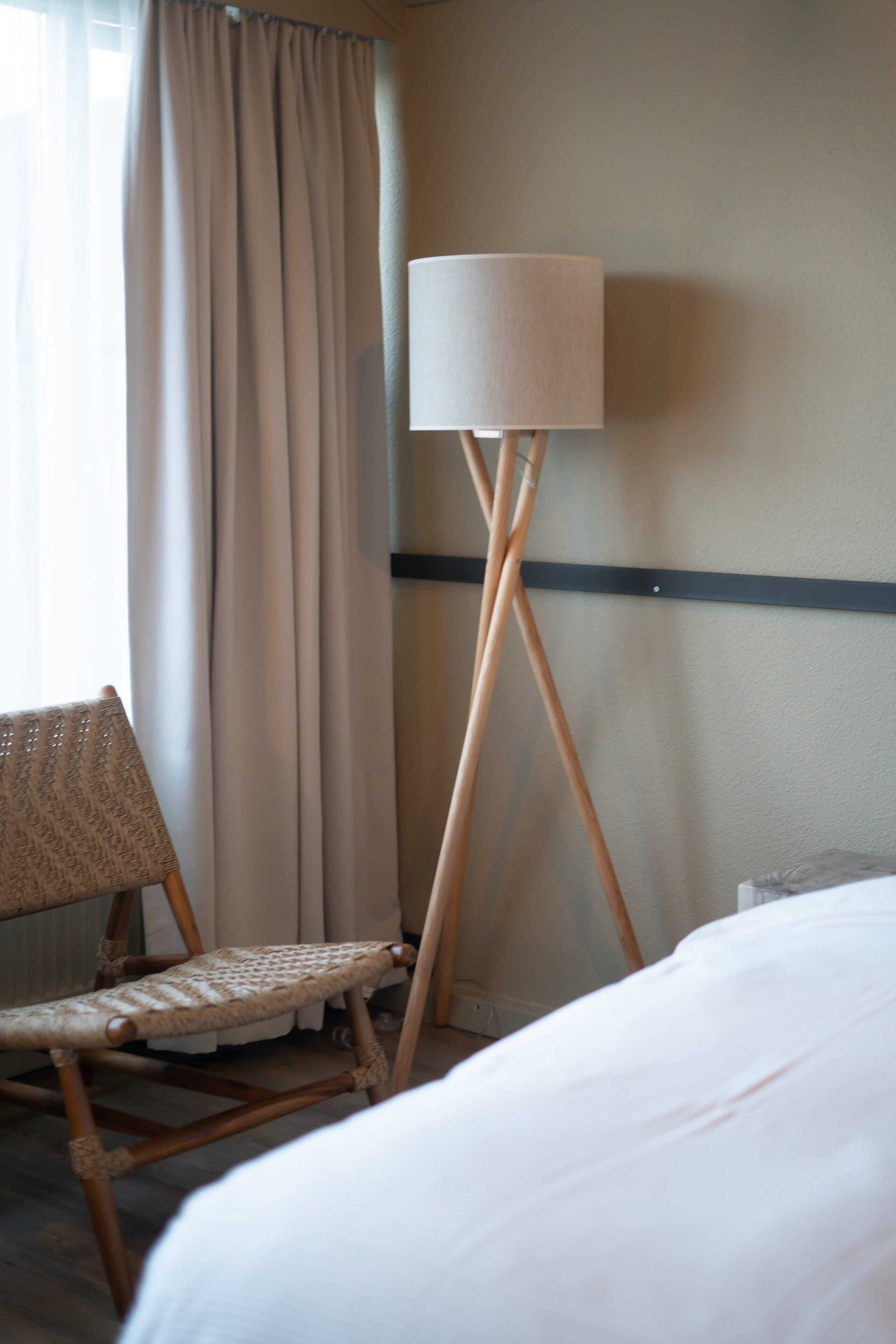 A room with a bed, a chair, a floor lamp, and a window with curtains.