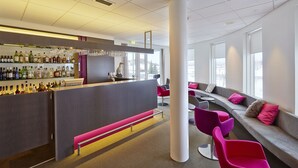 Un espace bar moderne avec un comptoir, des étagères remplies de bouteilles, et des sièges comprenant des chaises colorées et un banc.