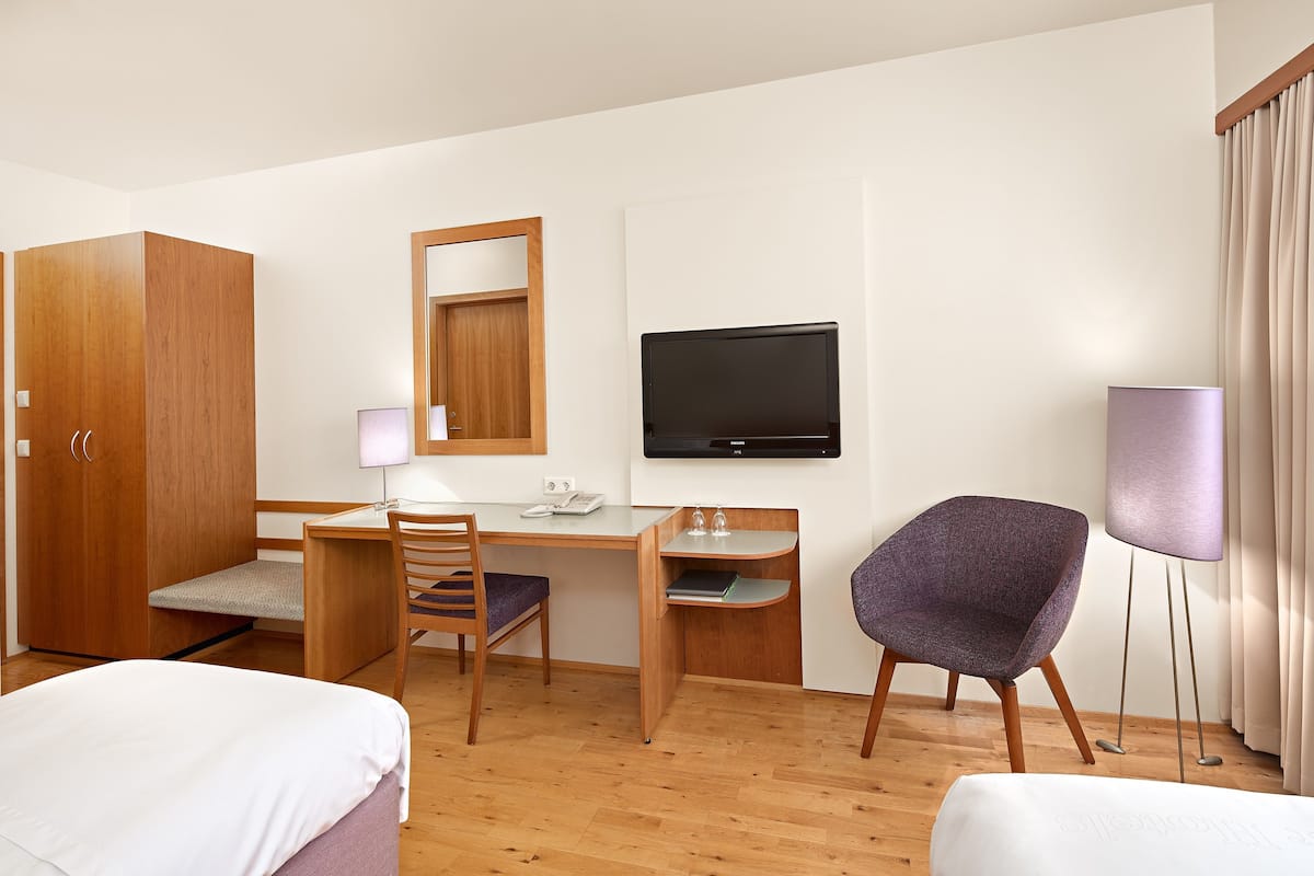Ein Hotelzimmer mit einem Holztisch, einem Fernseher, einem violetten Sessel, einem Bett und einem Kleiderschrank.