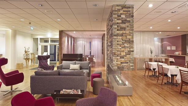 Un hall d’hôtel moderne doté d’un espace salon, d’un mur décoratif en pierre et d’un coin repas.