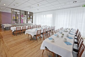 Une salle à manger d’hôtel avec de nombreuses tables dressées pour les clients, des chaises en bois et une grande bibliothèque contenant divers objets décoratifs.