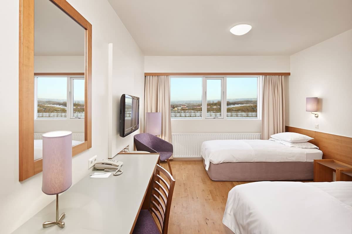 Een hotelkamer met een bed, een bureau met lamp, een televisie en uitzicht op het landschap.