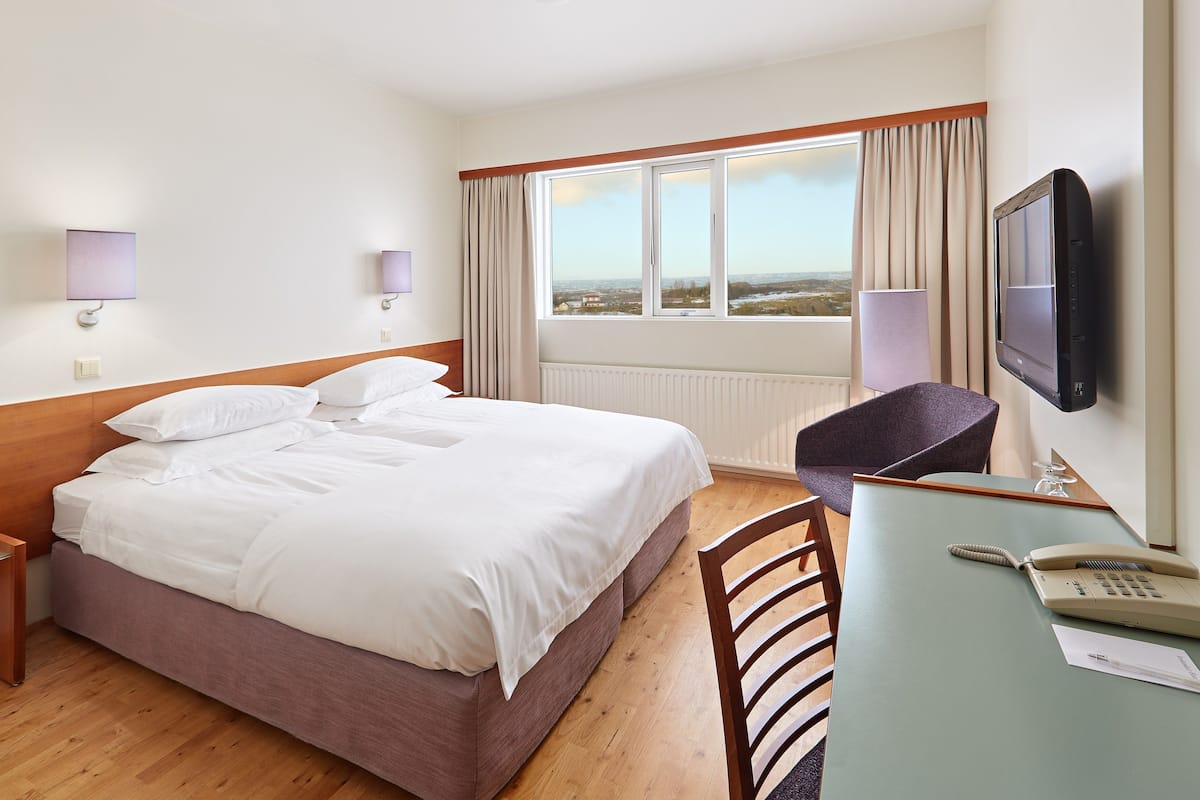 Ein Hotelzimmer mit einem Bett, einem Schreibtisch mit Telefon und einem an der Wand montierten Fernseher.