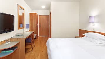 Una habitación de hotel con una cama, un escritorio con ordenador, televisor, espejo y puerta.