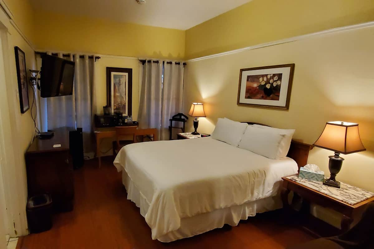 A hotel room with a bed, bedside lamps, a desk with a chair, a television, and a mirror.