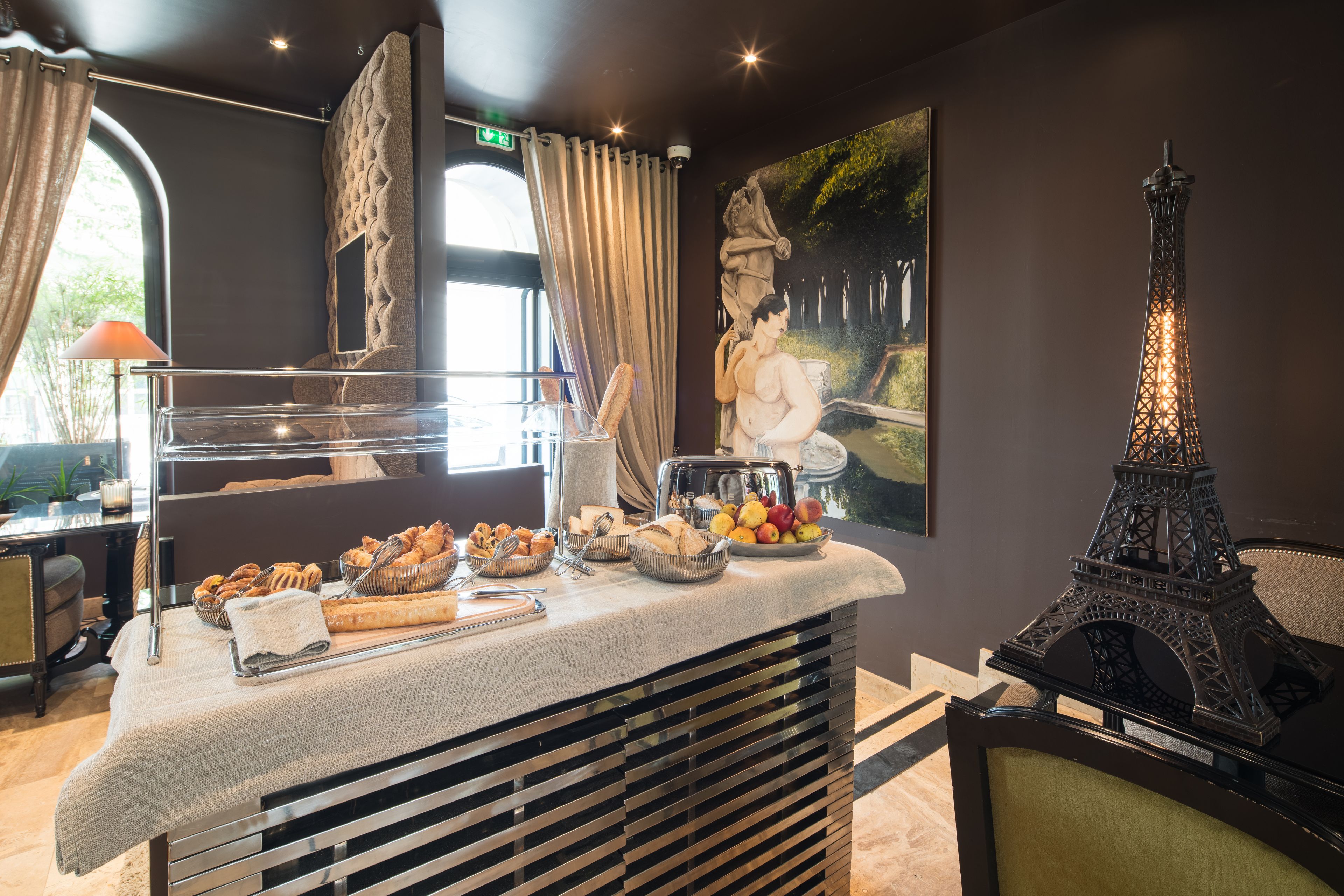 A breakfast buffet with various pastries and fruits, a decorative Eiffel Tower model, and a painting of a woman in a garden.