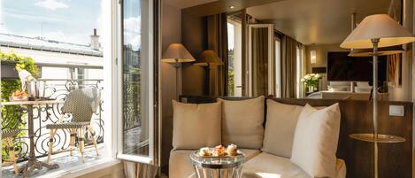A modern living room with a sofa, two lamps, a small table with pastries, and a balcony with outdoor furniture.