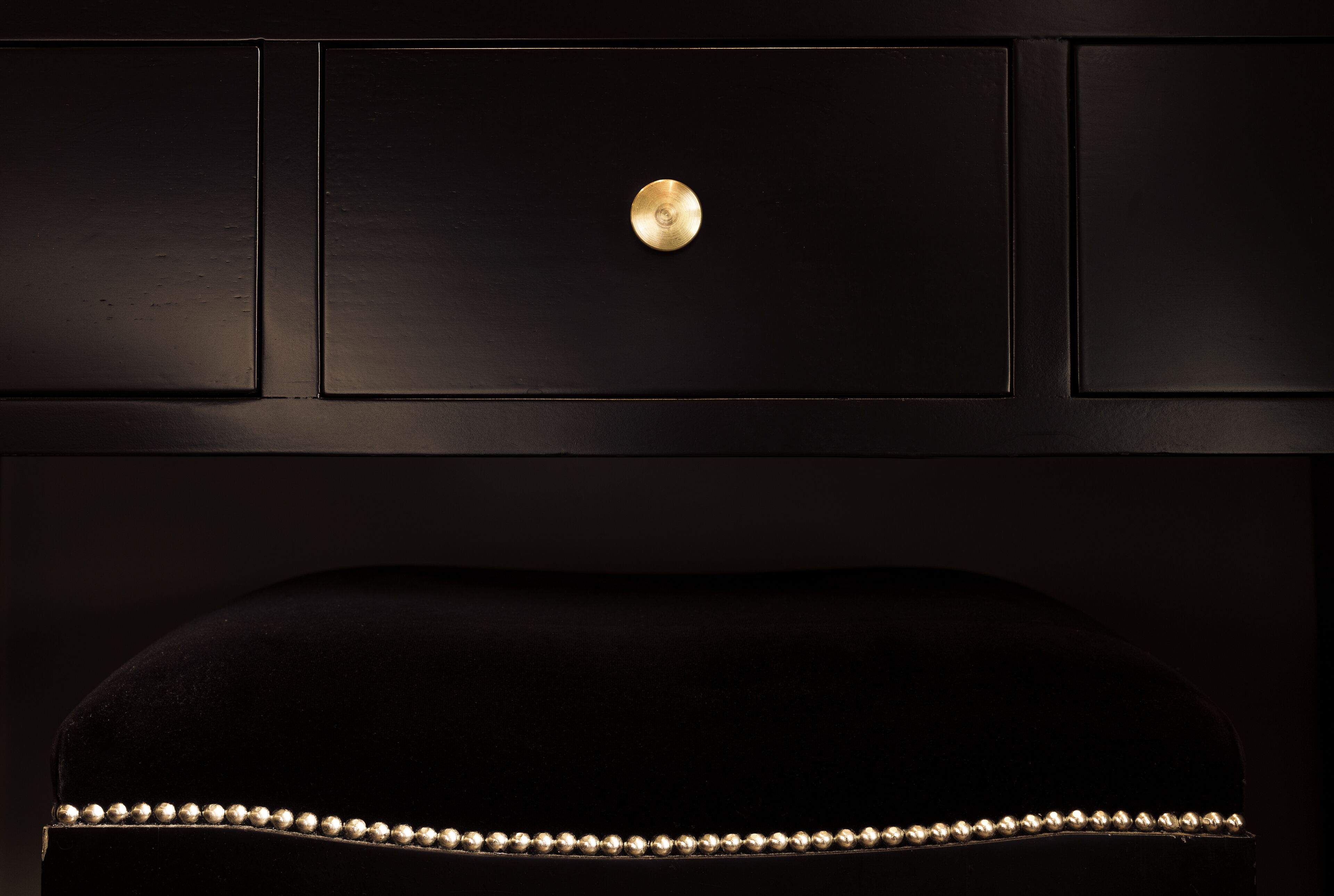 Un fauteuil noir recouvert de tissu, orné d’un bouton doré et d’une bordure à motifs.
