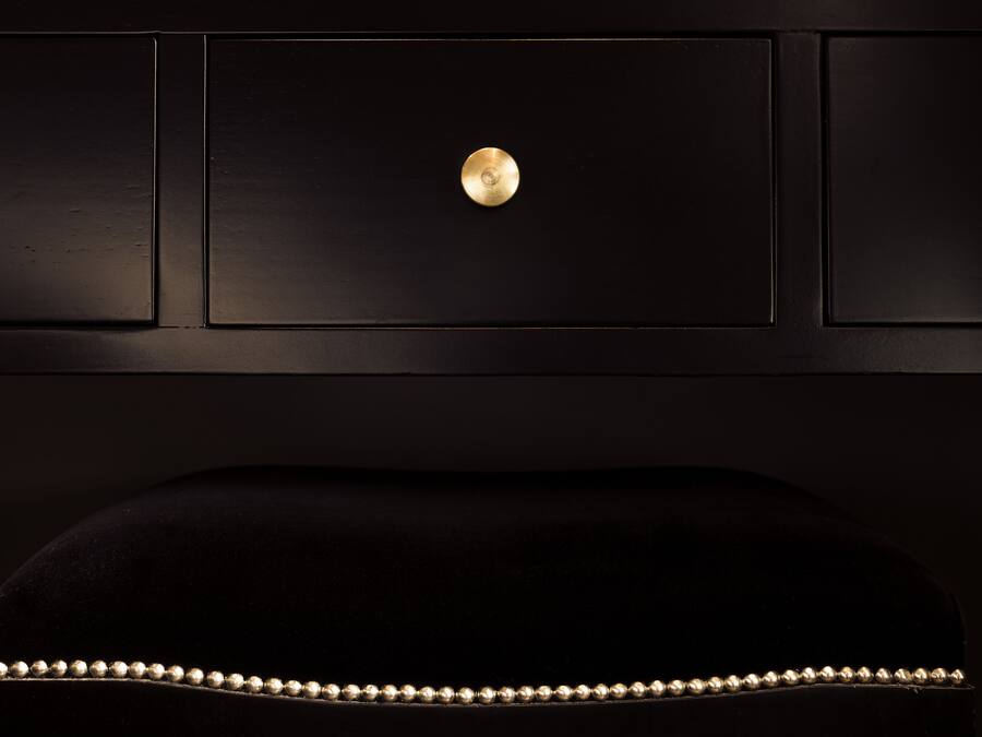 Un fauteuil noir recouvert de tissu, orné d’un bouton doré et d’une bordure à motifs.