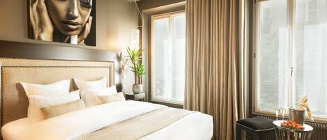 Habitación de hotel con una cama grande, una mesita con una bebida y vistas a la ciudad a través de amplios ventanales.