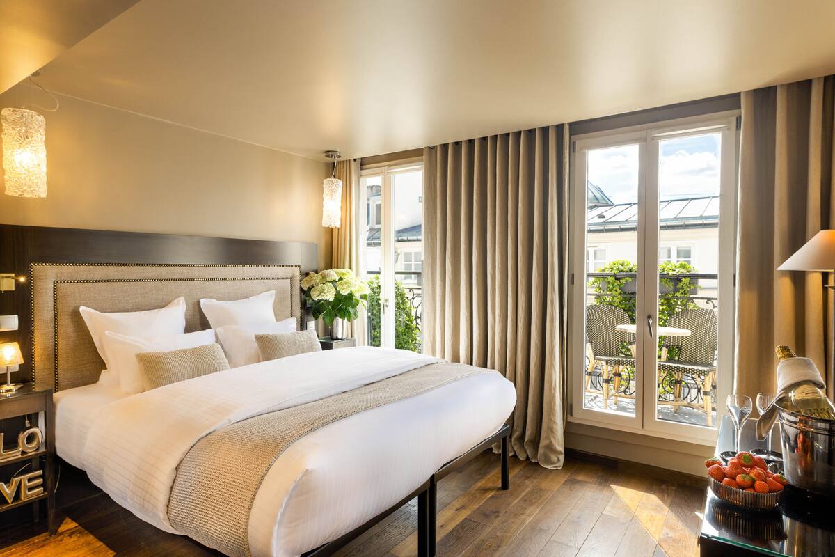 Quarto de hotel com uma cama grande, uma mesa de cabeceira com abajur, uma janela com cortinas e vista para o exterior.