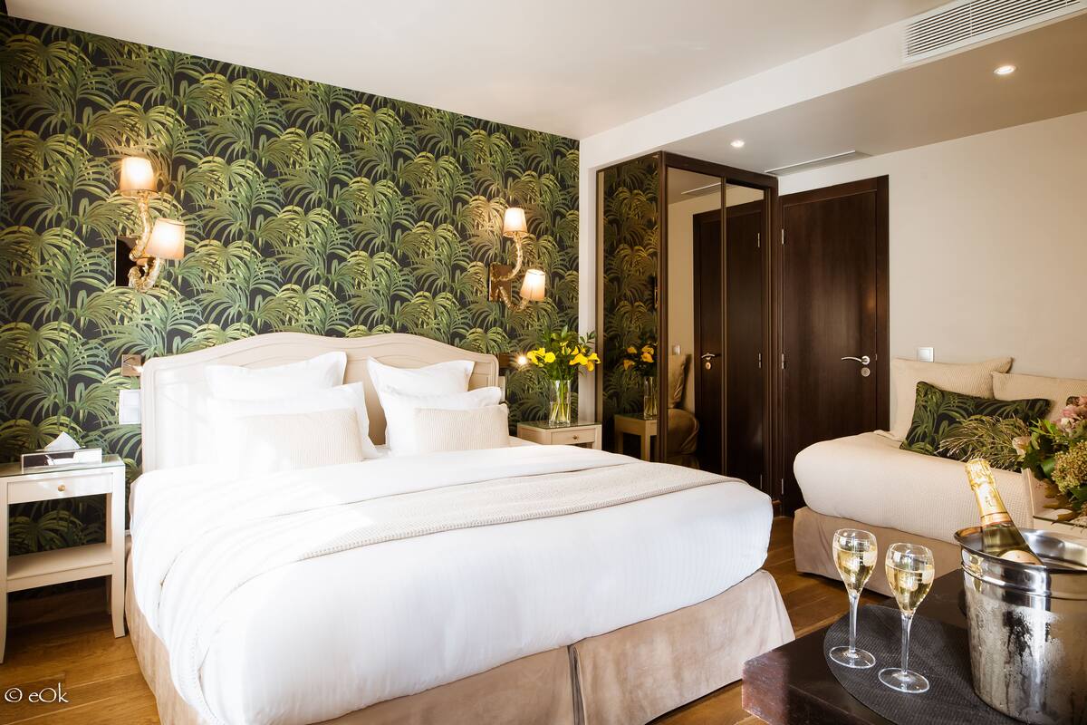 Quarto bem decorado com uma cama grande, mesas de cabeceira, um criado-mudo, cômoda, área de estar com sofá e uma garrafa de champanhe em um suporte.
