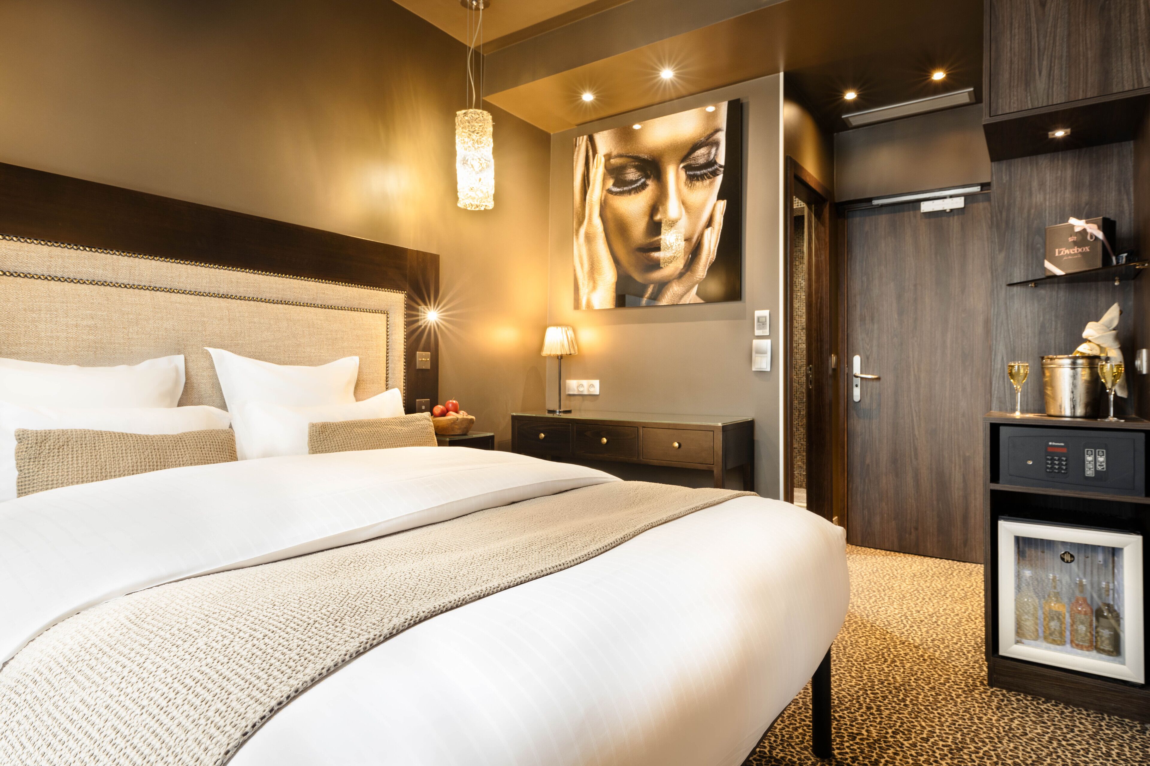 Una habitación de hotel moderna con una cama grande, una obra de arte en la pared, un minibar y un refrigerador pequeño.
