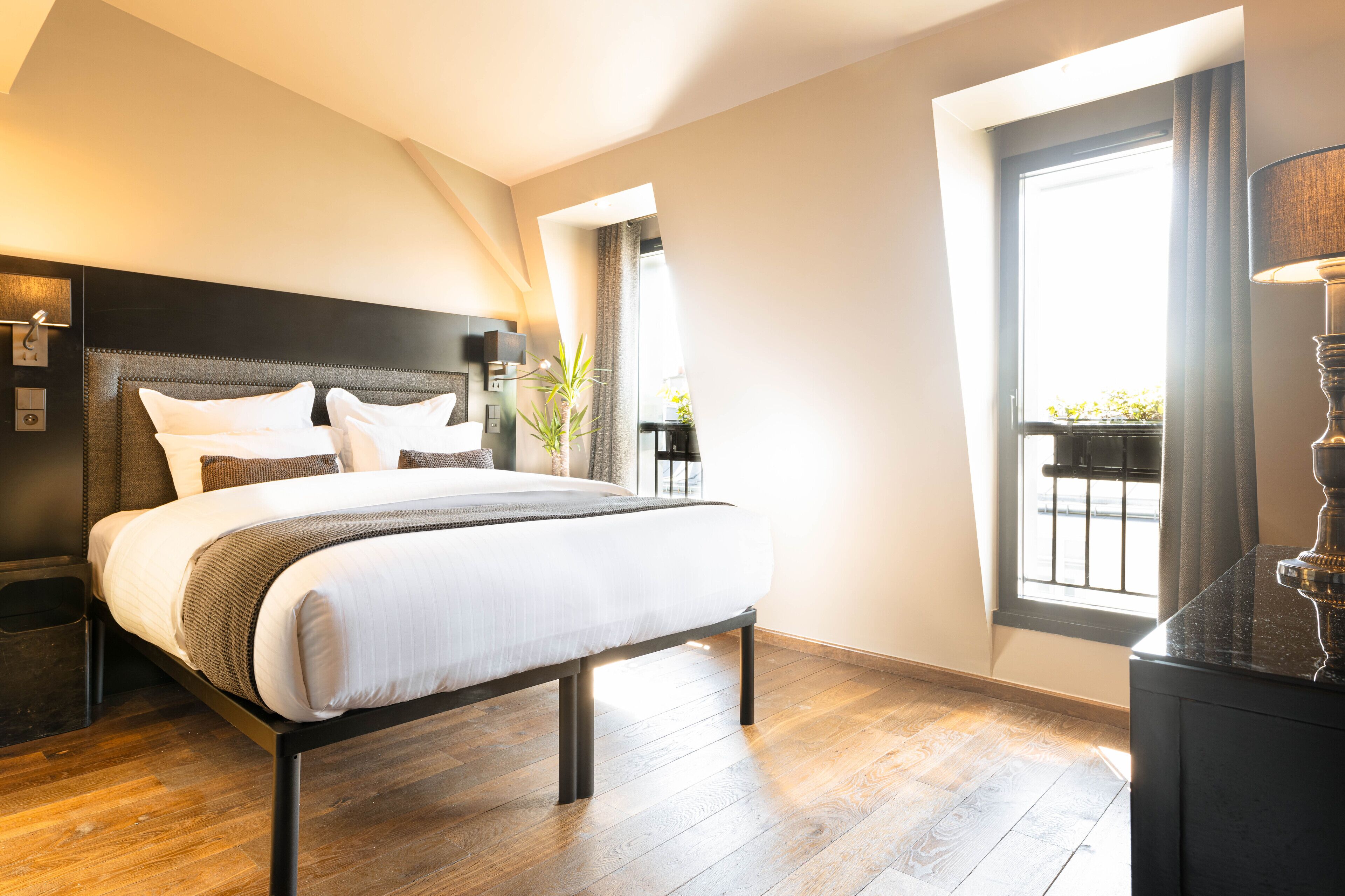 A modern bedroom with a large bed, a nightstand, a lamp, and a window with a view of the outside.