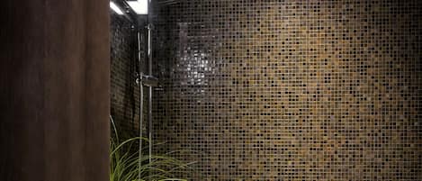 Un baño con pared de mosaicos, puerta de madera, lavamanos y zona de ducha.