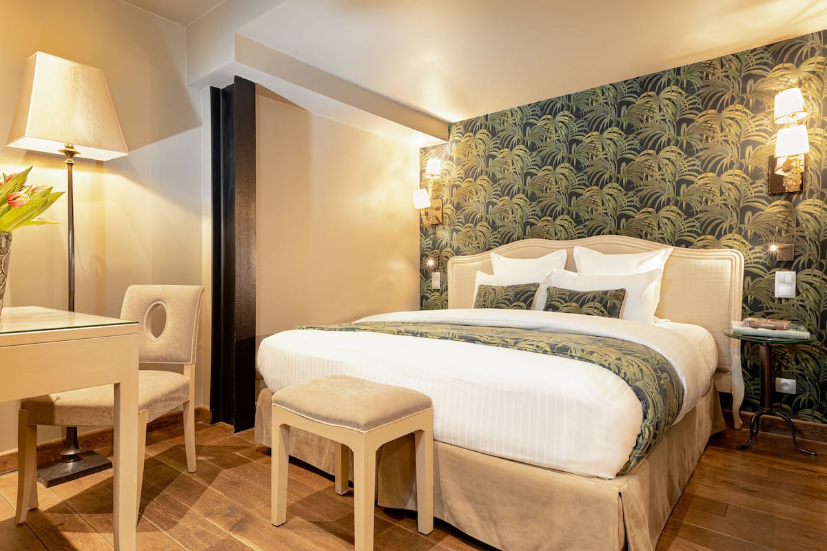 Quarto de hotel bem arrumado, com uma cama, uma cadeira, uma mesinha e um abajur.
