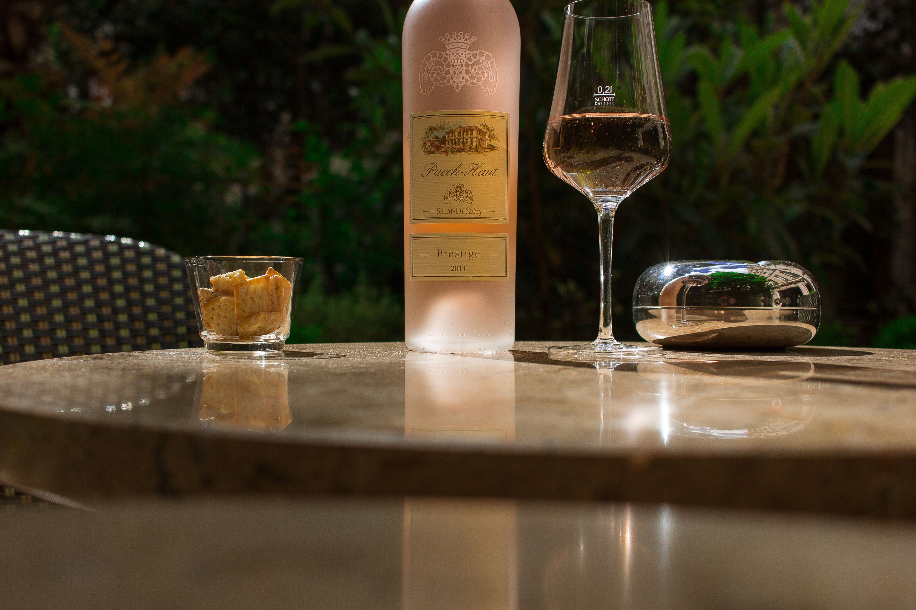 Een fles wijn, een glas en een kleine schaal op een ronde buitentafel.