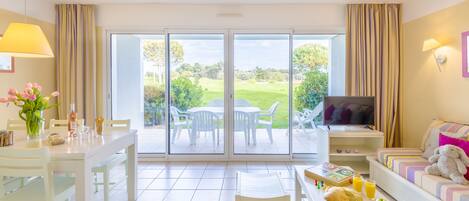 A bright room with a dining table, chairs, a sofa, and a TV.